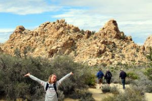 Ellie smiling with her hands and arms spread in front of a mountain