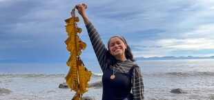 Lucero González Ruiz smiling big, holding up a piece of seaweed